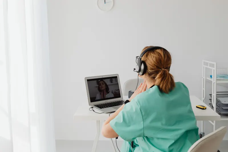 Profesional de salud con uniforme turquesa en una videollamada desde su consultorio.
